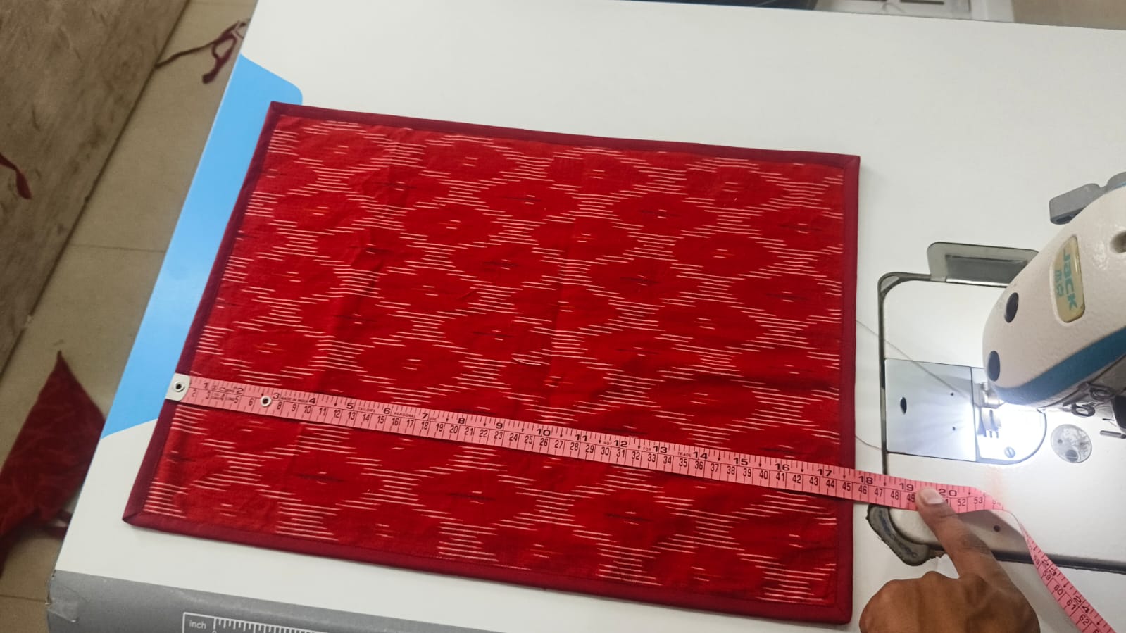 A red ikat placemat being measured at the workshop in India